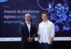 Siigo Aspel y la Asociación de Emprendedores de México (ASEM): digitalización empresarial impulsa ventas, productividad y competitividad Juan Carlos Cante, representante de la ASEM, y David Ortiz, CEO de Siigo Aspel, posan de pie lado a lado en un plano entero frente a una gran pantalla digital. Cante, a la izquierda, viste un traje sastre formal azul marino con camisa blanca de cuello abierto y mantiene las manos cruzadas al frente. Ortiz, a la derecha, posa sonriente con la mano izquierda en el bolsillo de su pantalón oscuro, vistiendo su camisa casual blanca. El fondo de la pantalla despliega el título del informe "Impacto de plataformas digitales en la gestión empresarial" flanqueado por gráficos isométricos en 3D de servidores, nube y analítica informática.