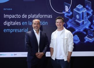 Siigo Aspel y la Asociación de Emprendedores de México (ASEM): digitalización empresarial impulsa ventas, productividad y competitividad Juan Carlos Cante, representante de la ASEM, y David Ortiz, CEO de Siigo Aspel, posan de pie lado a lado en un plano entero frente a una gran pantalla digital. Cante, a la izquierda, viste un traje sastre formal azul marino con camisa blanca de cuello abierto y mantiene las manos cruzadas al frente. Ortiz, a la derecha, posa sonriente con la mano izquierda en el bolsillo de su pantalón oscuro, vistiendo su camisa casual blanca. El fondo de la pantalla despliega el título del informe "Impacto de plataformas digitales en la gestión empresarial" flanqueado por gráficos isométricos en 3D de servidores, nube y analítica informática.