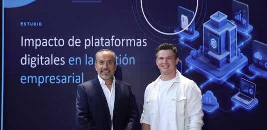 Siigo Aspel y la Asociación de Emprendedores de México (ASEM): digitalización empresarial impulsa ventas, productividad y competitividad Juan Carlos Cante, representante de la ASEM, y David Ortiz, CEO de Siigo Aspel, posan de pie lado a lado en un plano entero frente a una gran pantalla digital. Cante, a la izquierda, viste un traje sastre formal azul marino con camisa blanca de cuello abierto y mantiene las manos cruzadas al frente. Ortiz, a la derecha, posa sonriente con la mano izquierda en el bolsillo de su pantalón oscuro, vistiendo su camisa casual blanca. El fondo de la pantalla despliega el título del informe "Impacto de plataformas digitales en la gestión empresarial" flanqueado por gráficos isométricos en 3D de servidores, nube y analítica informática.