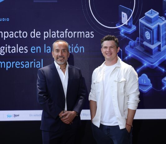 Siigo Aspel y la Asociación de Emprendedores de México (ASEM): digitalización empresarial impulsa ventas, productividad y competitividad Juan Carlos Cante, representante de la ASEM, y David Ortiz, CEO de Siigo Aspel, posan de pie lado a lado en un plano entero frente a una gran pantalla digital. Cante, a la izquierda, viste un traje sastre formal azul marino con camisa blanca de cuello abierto y mantiene las manos cruzadas al frente. Ortiz, a la derecha, posa sonriente con la mano izquierda en el bolsillo de su pantalón oscuro, vistiendo su camisa casual blanca. El fondo de la pantalla despliega el título del informe "Impacto de plataformas digitales en la gestión empresarial" flanqueado por gráficos isométricos en 3D de servidores, nube y analítica informática.