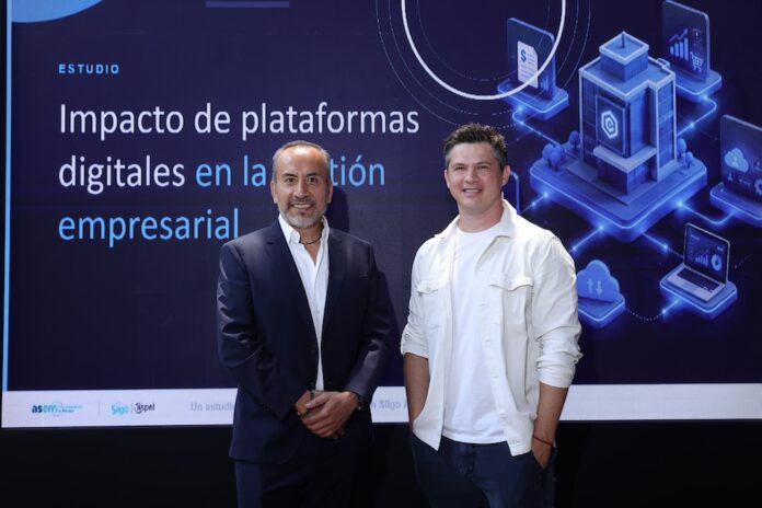 La ASEM y Siigo Aspel presentan una investigación conjunta sobre la madurez digital empresarial Juan Carlos Cante, representante de la ASEM, y David Ortiz, CEO de Siigo Aspel, posan de pie lado a lado en un plano entero frente a una gran pantalla digital. Cante, a la izquierda, viste un traje sastre formal azul marino con camisa blanca de cuello abierto y mantiene las manos cruzadas al frente. Ortiz, a la derecha, posa sonriente con la mano izquierda en el bolsillo de su pantalón oscuro, vistiendo su camisa casual blanca. El fondo de la pantalla despliega el título del informe