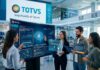TOTVS impulsa bases estratégicas para acelerar el éxito de la IA en América Latina Una imagen corporativa futurista de un equipo de TOTVS interactuando con paneles de datos y pantallas flotantes transparentes. En el centro, una pantalla grande de 'TOTVS AI' muestra gráficos e información sobre 'Recomendación de inventario Inteligente (RI)', 'TOTVS ERP' y 'Big Data'. Cuatro empleados usan dispositivos flotantes para visualizar planes de optimización de la cadena de suministro. Al fondo, un letrero de 'TOTVS' dice 'Impulsando el futuro' y muestra estadísticas de crecimiento. La escena está llena de símbolos tecnológicos y un brazo robótico en una mesa.