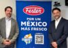 Fester y Google lanzan plataforma con IA para combatir las islas de calor urbano en México Fotografía en plano medio de estudio que muestra a dos ejecutivos de pie y sonrientes flanqueando una gran lona publicitaria de color azul brillante. El profesional de la izquierda, Sebastián Hiernaux de Google México, viste un saco gris claro sobre una camisa blanca de botones y pantalones de mezclilla; el directivo de la derecha, Vicente Madrid de Henkel, usa un traje sastre azul marino formal con camisa blanca. La mampara central despliega el logotipo ovalado de "Fester" en color rojo y blanco, seguido de la frase en letras blancas "POR UN MÉXICO MÁS FRESCO", un gráfico de la iniciativa "TECNOLOGÍA COOL ROOF" y un código QR grande con la leyenda "PRUEBA LA HERRAMIENTA AQUÍ".