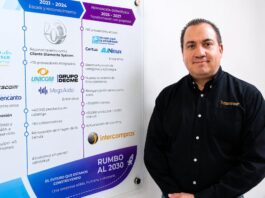 Intercompras: El eCommerce empresarial redefine la forma en que las organizaciones compran tecnología Retrato corporativo de plano medio que muestra a Eduardo Noriega, CEO de Intercompras, vistiendo una camisa negra formal con un sutil logotipo bordado en el pecho. Posa de tres cuartos hacia la izquierda, sonriendo levemente frente a una pared blanca donde cuelga un gran panel acrílico transparente. El panel despliega una línea de tiempo corporativa dividida en secciones cronológicas con logotipos de marcas como Cisco, Syscom, Unicom y Grupo Decme, detallando hitos de infraestructura, volumen de productos, cantidad de clientes y una sección inferior titulada "Rumbo al 2030: El futuro que estamos construyendo".