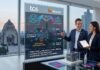 TCS y Mistral llevan la IA empresarial personalizada a una nueva etapa global Fotografía en plano medio de tres profesionales corporativos en trajes oscuros situados dentro de una oficina con una vista panorámica urbana del Monumento a la Revolución en la Ciudad de México a través del ventanal. En la sección izquierda, una pantalla vertical de cristal translúcido muestra diagramas informativos con los logotipos de "TCS" y "Mistral", desglosando sectores como Banca, Retail, Energía y Servicios Públicos bajo el concepto "IA específica por dominio". El ejecutivo central sonríe mientras apunta con su mano hacia la infografía del panel, al tiempo que una de las ejecutivas sostiene una tableta digital. En primer plano, sobre una mesa de vidrio, se aprecian folletos informativos y una pequeña maqueta de un centro de datos dentro de un cubo transparente.