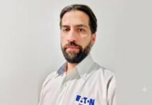 Eaton impulsa los UPS para infraestructura crítica con mayor disponibilidad, escalabilidad y eficiencia Fotografía de retrato en plano medio de Alejandro Lavín, Product Manager CPS de Eaton. El ejecutivo, de cabello oscuro, tez clara y barba, mira directamente a la cámara con una expresión neutral. Viste una camisa blanca de botones que lleva bordado el logotipo azul de la marca Eaton en el lado izquierdo del pecho, sobre un fondo liso de color gris claro.