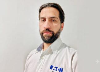 Eaton impulsa los UPS para infraestructura crítica con mayor disponibilidad, escalabilidad y eficiencia Fotografía de retrato en plano medio de Alejandro Lavín, Product Manager CPS de Eaton. El ejecutivo, de cabello oscuro, tez clara y barba, mira directamente a la cámara con una expresión neutral. Viste una camisa blanca de botones que lleva bordado el logotipo azul de la marca Eaton en el lado izquierdo del pecho, sobre un fondo liso de color gris claro.