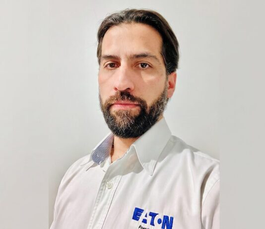 Eaton impulsa los UPS para infraestructura crítica con mayor disponibilidad, escalabilidad y eficiencia Fotografía de retrato en plano medio de Alejandro Lavín, Product Manager CPS de Eaton. El ejecutivo, de cabello oscuro, tez clara y barba, mira directamente a la cámara con una expresión neutral. Viste una camisa blanca de botones que lleva bordado el logotipo azul de la marca Eaton en el lado izquierdo del pecho, sobre un fondo liso de color gris claro.