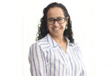 Sophos MDR acelera la respuesta a ciberamenazas con IA para fortalecer la resiliencia enterprise Retrato de estudio en plano medio y de frente de Daniela Arroyo, Channel Sales Engineer para LATAM en Sophos, posando sonriente sobre un fondo blanco uniforme. La especialista, de tez clara y cabello oscuro rizado de largo medio, usa anteojos de armazón negro, aretes colgantes plateados y una cadena delgada con un dije; viste una camisa blanca formal con líneas verticales azules y botones blancos.