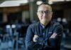 ManageEngine revela que las empresas mexicanas apuestan por consolidar TI para acelerar el valor de la inteligencia artificial Fotografía de medio cuerpo de un hombre, Wilson Calderón, que mira a la cámara con una expresión serena y profesional. Usa anteojos oscuros y una camisa negra de manga larga con el logotipo de ManageEngine bordado en el pecho. Mantiene los brazos cruzados y se encuentra de pie frente a un entorno de oficina que aparece completamente desenfocado en el fondo.