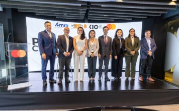 AMITI presenta “PyMEs Ciberseguras” para fortalecer la protección digital de empresas mexicanas Fotografía frontal de un grupo de ocho personas, conformado por hombres y mujeres en vestimenta formal de negocios, posando de pie y sonriendo sobre un escenario. A la izquierda del grupo hay un podio transparente que muestra el logotipo de Mastercard. En la parte trasera, una gran pantalla curva iluminada exhibe parte del texto del evento y los logotipos oficiales de AMITI, Capa 8, KIO IT Services y Mastercard.