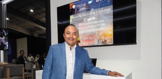 CeleriTech impulsa una nueva etapa para la inteligencia artificial empresarial Fotografía de Gonzalo Bretón, socio cofundador de CeleriTech, sonriendo a la cámara mientras apoya su mano izquierda sobre un módulo blanco con el logotipo naranja y gris de su empresa. Viste un saco azul claro y camisa blanca sin corbata, y se encuentra de pie frente a una gran pantalla que proyecta una presentación corporativa con los logotipos de CeleriTech y SAP.