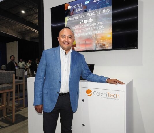 CeleriTech impulsa una nueva etapa para la inteligencia artificial empresarial Fotografía de Gonzalo Bretón, socio cofundador de CeleriTech, sonriendo a la cámara mientras apoya su mano izquierda sobre un módulo blanco con el logotipo naranja y gris de su empresa. Viste un saco azul claro y camisa blanca sin corbata, y se encuentra de pie frente a una gran pantalla que proyecta una presentación corporativa con los logotipos de CeleriTech y SAP.