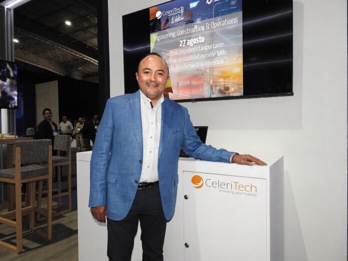 De la experimentación al retorno de inversión con Inteligencia Artificial Fotografía de Gonzalo Bretón, socio cofundador de CeleriTech, sonriendo a la cámara mientras apoya su mano izquierda sobre un módulo blanco con el logotipo naranja y gris de su empresa. Viste un saco azul claro y camisa blanca sin corbata, y se encuentra de pie frente a una gran pantalla que proyecta una presentación corporativa con los logotipos de CeleriTech y SAP.