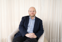 Ignia Cloud impulsa una operación de TI predictiva con servicios administrados e IA Retrato fotográfico de Esteban Rey, CEO de Ignia Cloud, sentado cómodamente en un sillón de tono claro. Viste una camisa a cuadros azules y blancos bajo un saco azul marino, lleva gafas de armazón transparente y mira de frente a la cámara con un fondo iluminado por cortinas blancas translúcidas.
