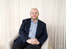Ignia Cloud impulsa una operación de TI predictiva con servicios administrados e IA Retrato fotográfico de Esteban Rey, CEO de Ignia Cloud, sentado cómodamente en un sillón de tono claro. Viste una camisa a cuadros azules y blancos bajo un saco azul marino, lleva gafas de armazón transparente y mira de frente a la cámara con un fondo iluminado por cortinas blancas translúcidas.
