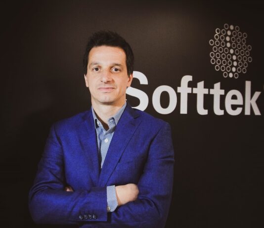 Softtek: el CIO redefine su rol y convierte la tecnología en una decisión económica Fotografía de medio cuerpo de Juan José D'Alessandro posando con los brazos cruzados. Viste una camisa de patrón claro y un saco azul, ubicado frente a un fondo oscuro donde destaca el logotipo corporativo de la empresa Softtek.