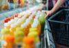 SAP destaca la sostenibilidad operativa como ventaja competitiva para las empresas Fotografía en primer plano de la mano de un comprador tomando una botella de jugo verde de una repisa refrigerada en un supermercado para colocarla dentro de una canasta de compras negra.