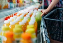 SAP destaca la sostenibilidad operativa como ventaja competitiva para las empresas Fotografía en primer plano de la mano de un comprador tomando una botella de jugo verde de una repisa refrigerada en un supermercado para colocarla dentro de una canasta de compras negra.