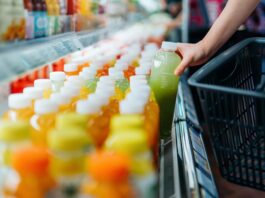 SAP destaca la sostenibilidad operativa como ventaja competitiva para las empresas Fotografía en primer plano de la mano de un comprador tomando una botella de jugo verde de una repisa refrigerada en un supermercado para colocarla dentro de una canasta de compras negra.