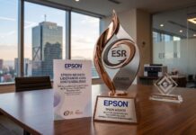 Epson México reafirma su compromiso con la sostenibilidad con el Distintivo ESR 2026 Fotografía de un premio metálico con el logotipo ESR y la inscripción CEMEFI sobre una mesa de juntas de madera. En la base del galardón se lee "EPSON MÉXICO RECEPTOR DESTACADO DEL DISTINTIVO ESR 2026". A su lado hay un folleto con el título "Epson México: Liderando con sostenibilidad" y un bloque de cristal decorativo. Al fondo, a través del amplio ventanal de la oficina, se aprecia la silueta del edificio del World Trade Center en la Ciudad de México durante el atardecer.