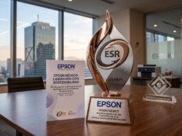 Epson México reafirma su compromiso con la sostenibilidad con el Distintivo ESR 2026 Fotografía de un premio metálico con el logotipo ESR y la inscripción CEMEFI sobre una mesa de juntas de madera. En la base del galardón se lee "EPSON MÉXICO RECEPTOR DESTACADO DEL DISTINTIVO ESR 2026". A su lado hay un folleto con el título "Epson México: Liderando con sostenibilidad" y un bloque de cristal decorativo. Al fondo, a través del amplio ventanal de la oficina, se aprecia la silueta del edificio del World Trade Center en la Ciudad de México durante el atardecer.