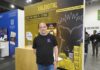 XalDigital apuesta por la transformación digital enterprise Fotografía de un directivo posando frente al stand corporativo de XalDigital, donde se exhibe su insignia como AWS Premier Partner. El módulo, diseñado en colores amarillo y negro, destaca los servicios de la compañía e incluye el mensaje "Construyendo el futuro", acompañado de gráficos urbanos y la mascota de la empresa.