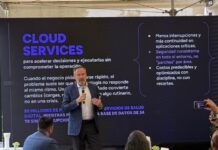 KIO IT Services revela las lecciones tecnológicas que dejó el Mundial 2026 Fotografía de Bruno Juanes hablando por micrófono frente a una pantalla oscura de presentación que resalta el texto "CLOUD SERVICES" y sus beneficios operativos, mientras miembros de la audiencia lo escuchan y graban con sus teléfonos móviles.