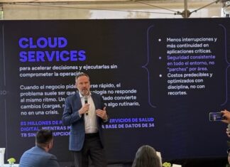 KIO IT Services revela las lecciones tecnológicas que dejó el Mundial 2026 Fotografía de Bruno Juanes hablando por micrófono frente a una pantalla oscura de presentación que resalta el texto "CLOUD SERVICES" y sus beneficios operativos, mientras miembros de la audiencia lo escuchan y graban con sus teléfonos móviles.