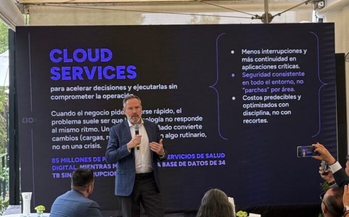 KIO IT Services y la evolución hacia una operación resiliente Fotografía de Bruno Juanes hablando por micrófono frente a una pantalla oscura de presentación que resalta el texto