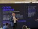KIO IT Services revela las lecciones tecnológicas que dejó el Mundial 2026 Fotografía de Bruno Juanes hablando por micrófono frente a una pantalla oscura de presentación que resalta el texto "CLOUD SERVICES" y sus beneficios operativos, mientras miembros de la audiencia lo escuchan y graban con sus teléfonos móviles.