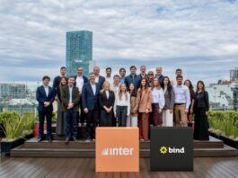 Inter desembarca en la Argentina con una plataforma integral para inversiones internacionales Fotografía de grupo al aire libre en una terraza donde ejecutivos y ejecutivas posan sonrientes organizados en dos filas. En el primer plano destacan dos tótems cúbicos: uno de color naranja con el logotipo de Inter y otro de color negro con la marca Bind, con edificios urbanos de fondo bajo un cielo nublado.