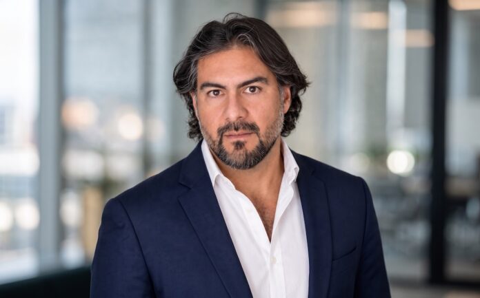 México lidera el mercado de Inteligencia Artificial empresarial en América Latina Retrato corporativo de Fernando Aldana posando en primer plano con saco azul marino sobre una camisa blanca. Se encuentra mirando fijamente a la cámara con una expresión seria y profesional dentro de un espacio de oficinas bien iluminado.