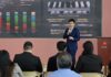Huawei impulsa la inteligencia artificial y el almacenamiento solar para la industria en México Fotografía de una presentación ejecutiva donde Zhou Bo habla con un micrófono de mano ante un auditorio. De fondo se aprecia una pantalla proyectora con gráficos estadísticos, mapas de plantas BESS y el logotipo corporativo de Huawei.