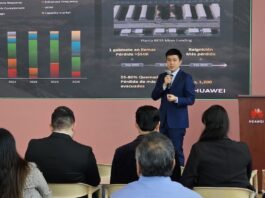 Huawei impulsa la inteligencia artificial y el almacenamiento solar para la industria en México Fotografía de una presentación ejecutiva donde Zhou Bo habla con un micrófono de mano ante un auditorio. De fondo se aprecia una pantalla proyectora con gráficos estadísticos, mapas de plantas BESS y el logotipo corporativo de Huawei.