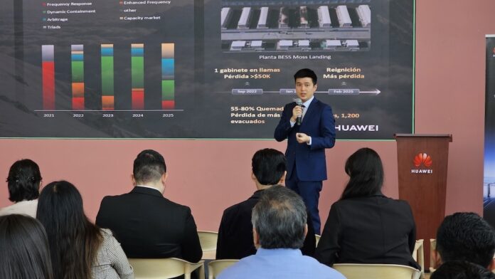 Fotografía de una presentación ejecutiva donde Zhou Bo habla con un micrófono de mano ante un auditorio. De fondo se aprecia una pantalla proyectora con gráficos estadísticos, mapas de plantas BESS y el logotipo corporativo de Huawei.