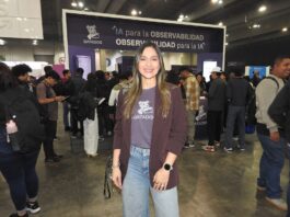 El poder de DataDog para asegurar el futuro de la inteligencia artificial empresarial Fotografía en plano medio de Queennie López, Senior Alliances Manager para Datadog en México, sonriendo frente al estand de la marca en un evento tecnológico con el lema "IA para la observabilidad, OBSERVABILIDAD para la IA" al fondo.