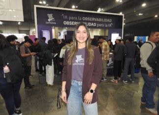El poder de DataDog para asegurar el futuro de la inteligencia artificial empresarial Fotografía en plano medio de Queennie López, Senior Alliances Manager para Datadog en México, sonriendo frente al estand de la marca en un evento tecnológico con el lema "IA para la observabilidad, OBSERVABILIDAD para la IA" al fondo.