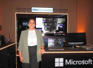 Dell Technologies y la revolución empresarial: inteligencia artificial a la medida con AMD Fotografía de plano medio de Margarita Gutiérrez posando sonriente en traje ejecutivo verde claro frente a un stand de exhibición tecnológica iluminado. Sobre la barra del stand se observa una computadora portátil y un monitor empresarial encendidos, acompañados por el letrero de Dell Technologies en la parte superior y el logotipo de Microsoft en el panel frontal inferior.