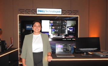 Dell Technologies y la revolución empresarial: inteligencia artificial a la medida con AMD Fotografía de plano medio de Margarita Gutiérrez posando sonriente en traje ejecutivo verde claro frente a un stand de exhibición tecnológica iluminado. Sobre la barra del stand se observa una computadora portátil y un monitor empresarial encendidos, acompañados por el letrero de Dell Technologies en la parte superior y el logotipo de Microsoft en el panel frontal inferior.