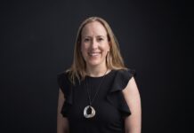 Mendel: De comprobantes perdidos a mejores decisiones; el papel de la IA Fotografía de retrato corporativo en plano medio de Ana María Ponce de León, CFO de Mendel, vestida con blusa negra sin mangas de holanes y collar metálico circular, sonriendo frente a un fondo negro neutro.