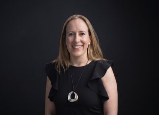 Mendel: De comprobantes perdidos a mejores decisiones; el papel de la IA Fotografía de retrato corporativo en plano medio de Ana María Ponce de León, CFO de Mendel, vestida con blusa negra sin mangas de holanes y collar metálico circular, sonriendo frente a un fondo negro neutro.