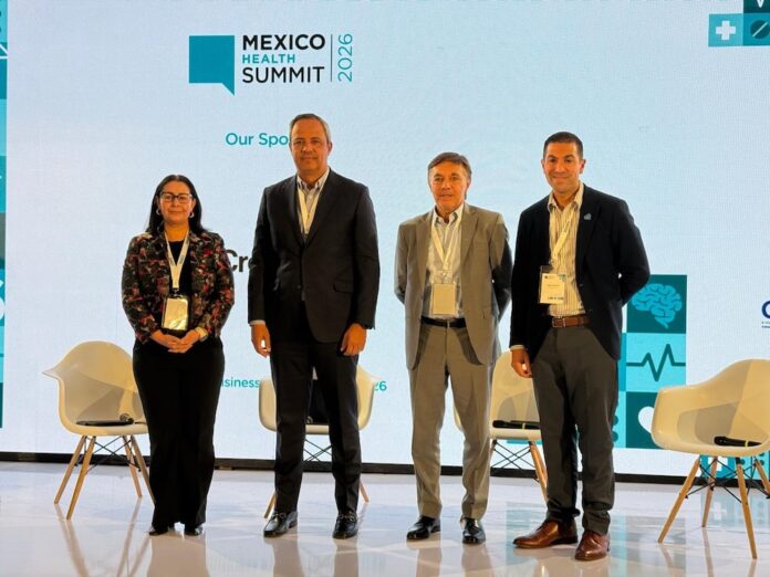 Especialistas y líderes del sector sanitario se reúnen en el Mexico Health Summit 2026 Fotografía de grupo en plano medio de cuatro ejecutivos y especialistas del sector salud posando de pie en el escenario del Mexico Health Summit 2026 frente al panel institucional del evento.
