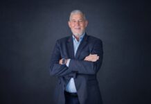 Ivanti: La automatización no es suficiente; la autonomía de TI también debe saber cuándo detenerse Fotografía de retrato corporativo en plano medio de Max Mayorga, Vicepresidente para América Latina de Ivanti, vistiendo saco azul marino sobre camisa azul claro, posando sonriente con los brazos cruzados frente a un fondo gris neutro.