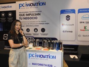 Fotografía en plano medio de Nadia González, Directora Operativa en corporativo PC Software, posando sonriente junto a muestras de promocionales y el módulo de atención de "PC Innovation".