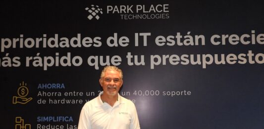 El salvavidas del centro de datos corporativo se llama Park Place y redefine la inversión tecnológica Fotografía en plano medio de Rogelio Moncada, Director Comercial para North Latam en Park Place Technologies, vistiendo camisa blanca tipo polo corporativa, posando sonriente frente a un muro publicitario con la frase "Las prioridades de IT están creciendo más rápido que tu presupuesto".
