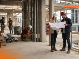 Cómo GAYA impulsa la IA y la gestión digital para anticipar sobrecostos en la construcción Fotografía en plano entero de dos ingenieros en obra revisando planos en papel con cascos de seguridad, mientras otros trabajadores realizan labores de construcción al fondo dentro de una estructura de concreto.