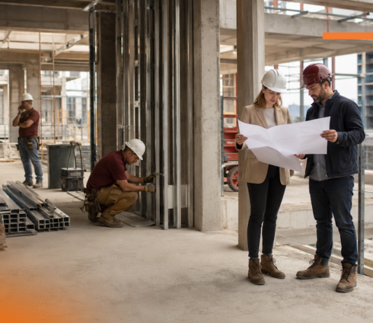Cómo GAYA impulsa la IA y la gestión digital para anticipar sobrecostos en la construcción Fotografía en plano entero de dos ingenieros en obra revisando planos en papel con cascos de seguridad, mientras otros trabajadores realizan labores de construcción al fondo dentro de una estructura de concreto.