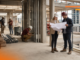 Cómo GAYA impulsa la IA y la gestión digital para anticipar sobrecostos en la construcción Fotografía en plano entero de dos ingenieros en obra revisando planos en papel con cascos de seguridad, mientras otros trabajadores realizan labores de construcción al fondo dentro de una estructura de concreto.